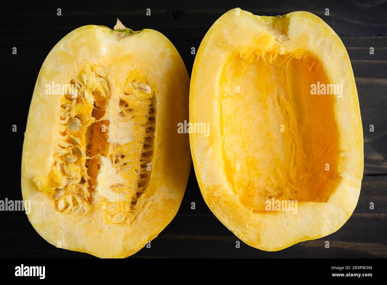 Squash di spaghetti a fette con semi laterali: Squash di spaghetti tagliato a metà con e senza semi da vicino su un tavolo di legno Foto Stock