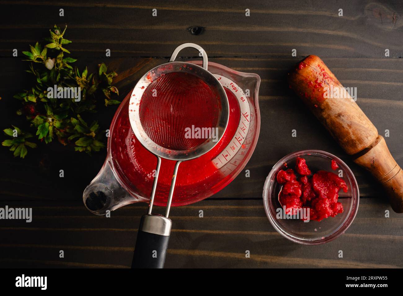 Filtrare la purea di fragole con un filtro a rete: Preparare una purea di fragole con un piccolo recipiente di semi sul lato Foto Stock