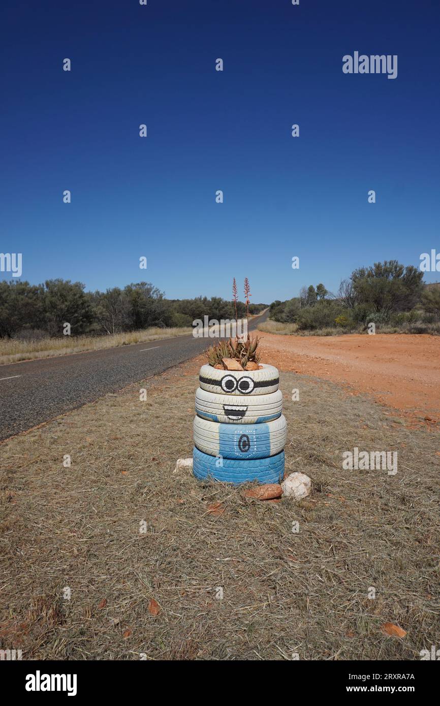 Un vaso di piante fatto di pneumatici di gomma per auto dipinte come un minion tratto dal film Dregicable me lungo la strada rurale nell'entroterra australiano Foto Stock