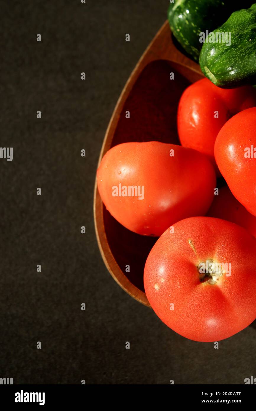 Pomodori freschi e cetrioli su piatto di legno, tavolo da cucina grigio scuro Foto Stock