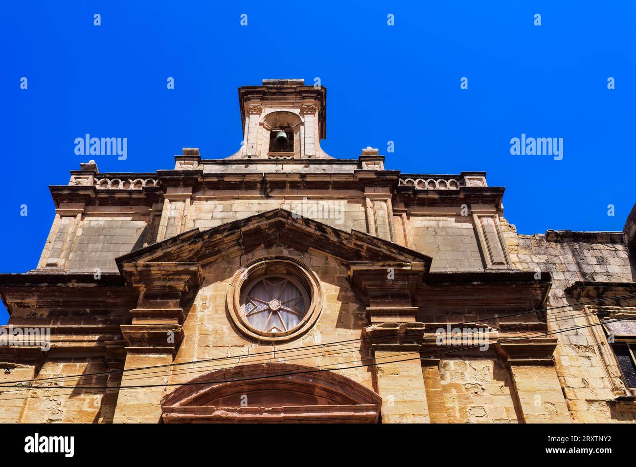 Esterno dell'Oratorio di Santa Croce di Malta con pietra calcarea, croce maltese e campanile sotto un cielo blu brillante, città vecchia di Birgu (città Vittoriosa) Foto Stock