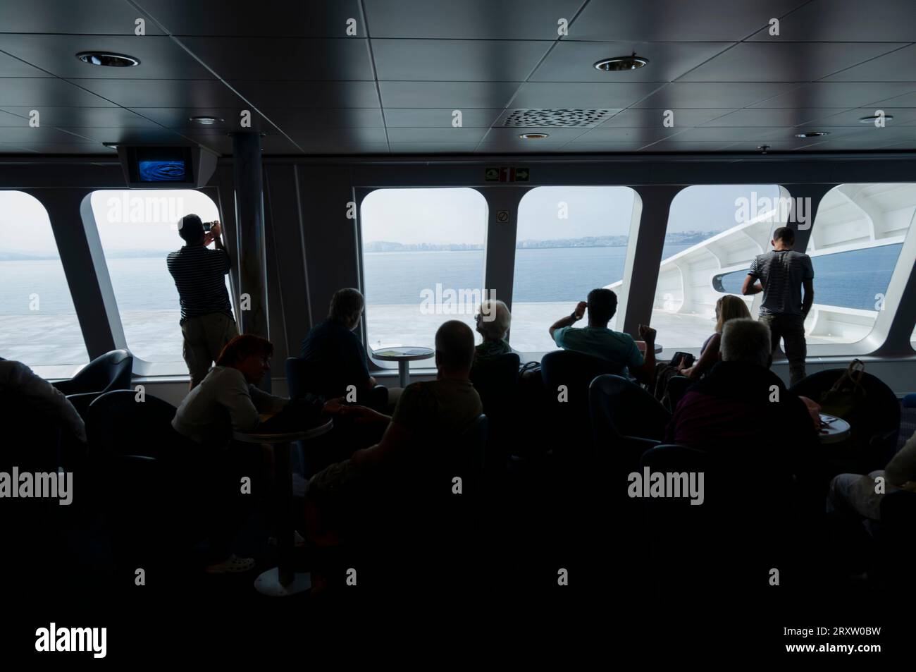 Silhouette di un gruppo di passeggeri su un traghetto mentre guardano attraverso i finestrini del ponte della nave vicino alla costa del Marocco Foto Stock
