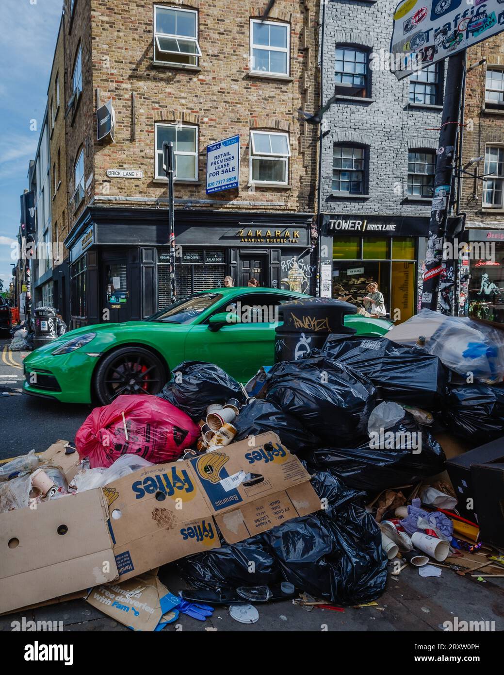 Un'auto veloce passa attraverso i rifiuti accumulati sul Brick Lane di Londra a Tower Hamlets. Foto Stock