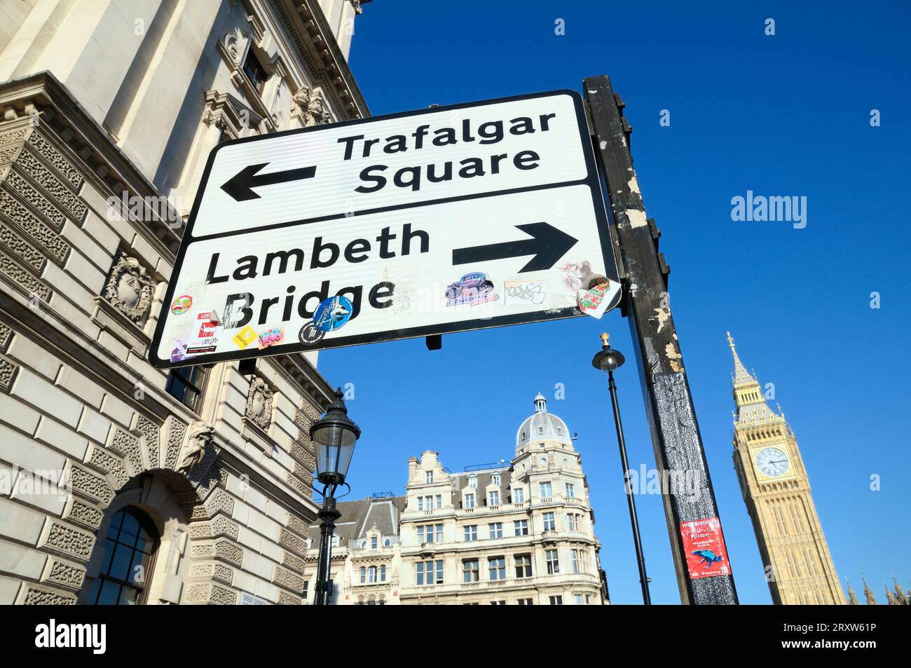 Indicazioni stradali per Londra con le frecce per Trafalgar Square e Lambeth Bridge. Adesivi d'arte visibili utilizzati dagli artisti di strada per promuovere il loro lavoro. Foto Stock