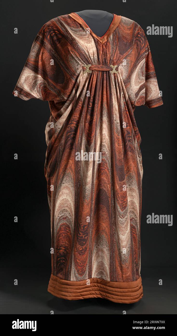 Questo vestito è stato indossato da Isabel Sanford come personaggio Louise Jefferson nello show televisivo "The Jeffersons". Il maxi dress è realizzato in tessuto in maglia sintetica con un design marrone, ruggine e beige con strisce macchiate che si alternano rivolte verso l'alto e verso il basso. Il collare è un collo a V sia nella parte anteriore che posteriore ed è delimitato da due strisce di tessuto a maglia sintetica in marrone massello e ruggine. Lo stesso tessuto marrone è cucito all'orlo in una fascia larga quattro (4) pollici, piegata sul retro per formare uno strato doppio e trapuntata con cinque (5) linee parallele orizzontali. Sull'esterno Foto Stock