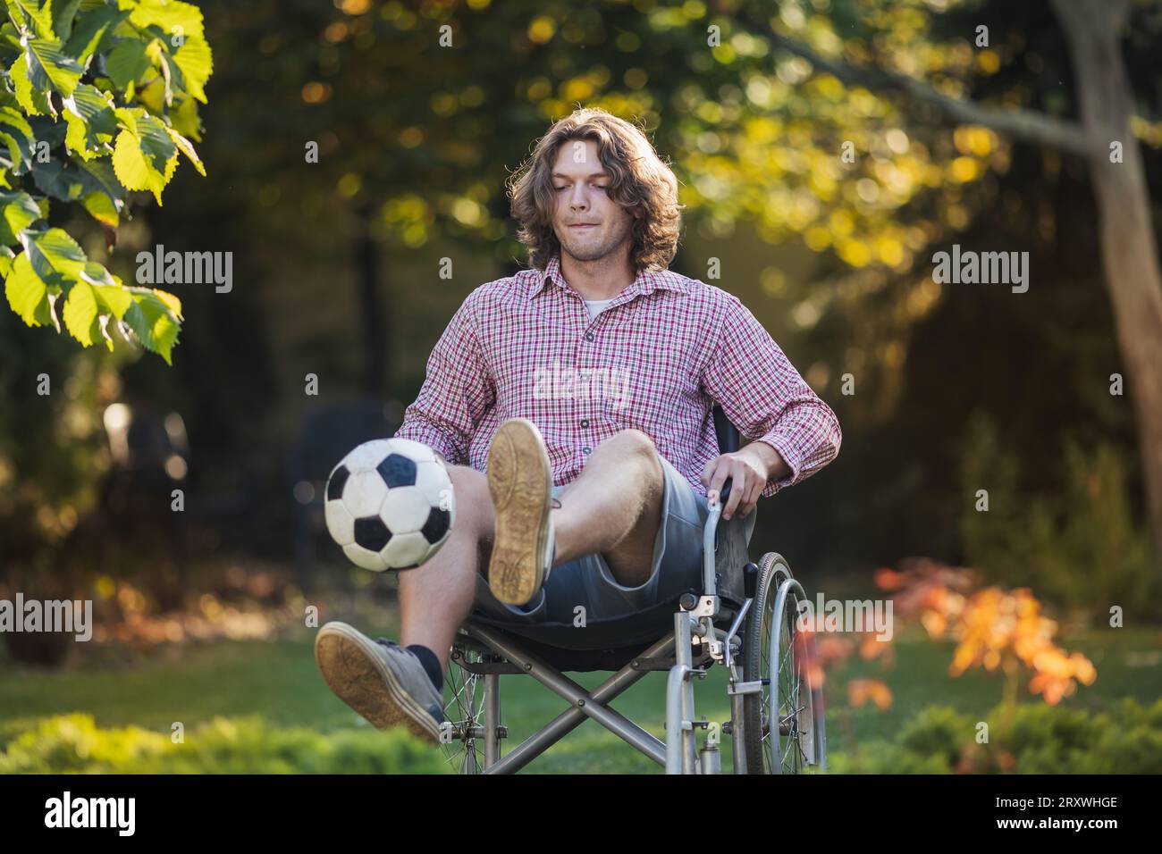 Giovane seduto in sedia a rotelle che ha un programma di riabilitazione dopo un infortunio e si esercita con il calcio Foto Stock