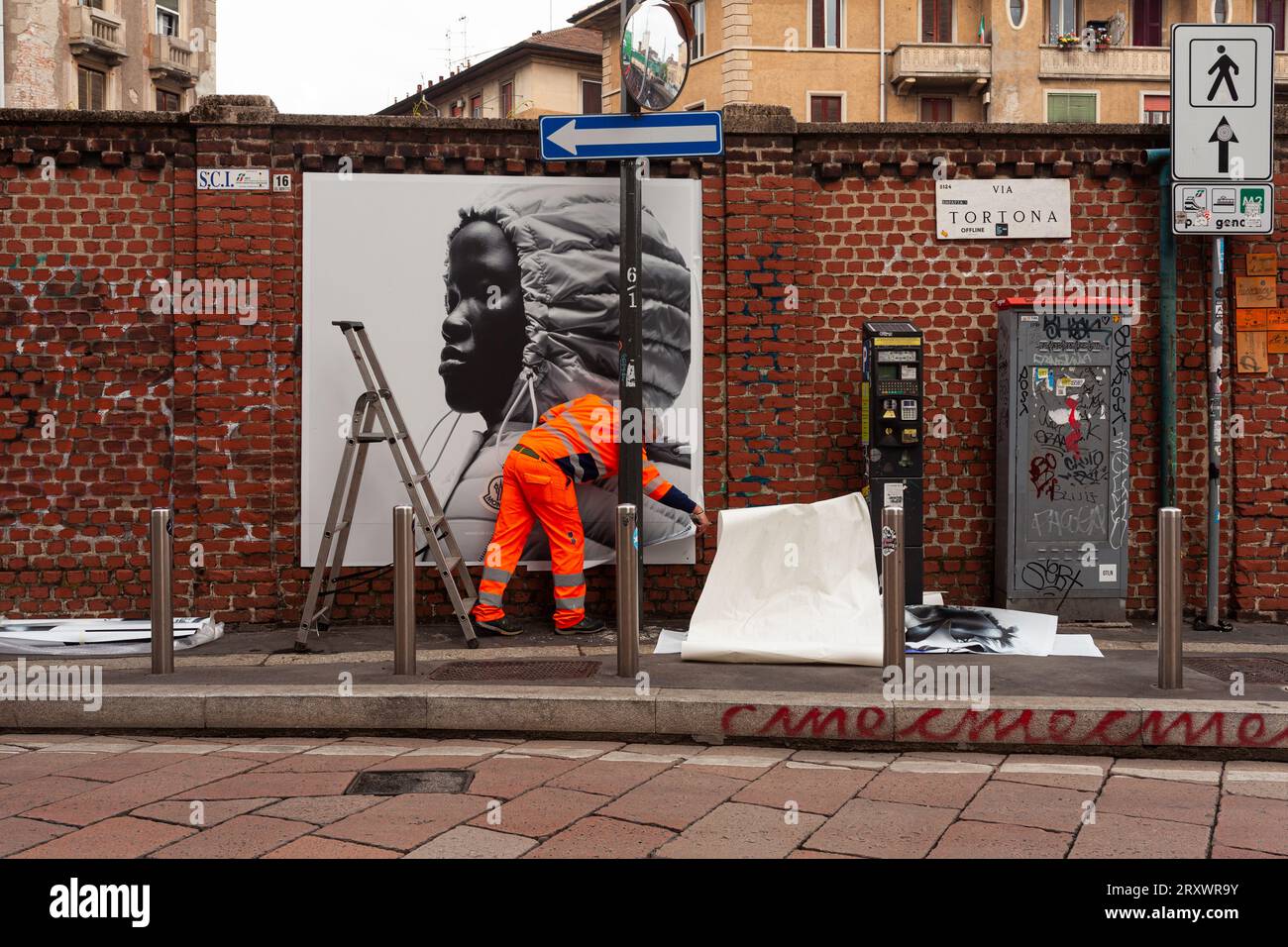 Milano, Italia - 21 aprile 2023: Un lavoratore sta mettendo sui muri dei manifesti della collezione Moncler del 2023 Foto Stock