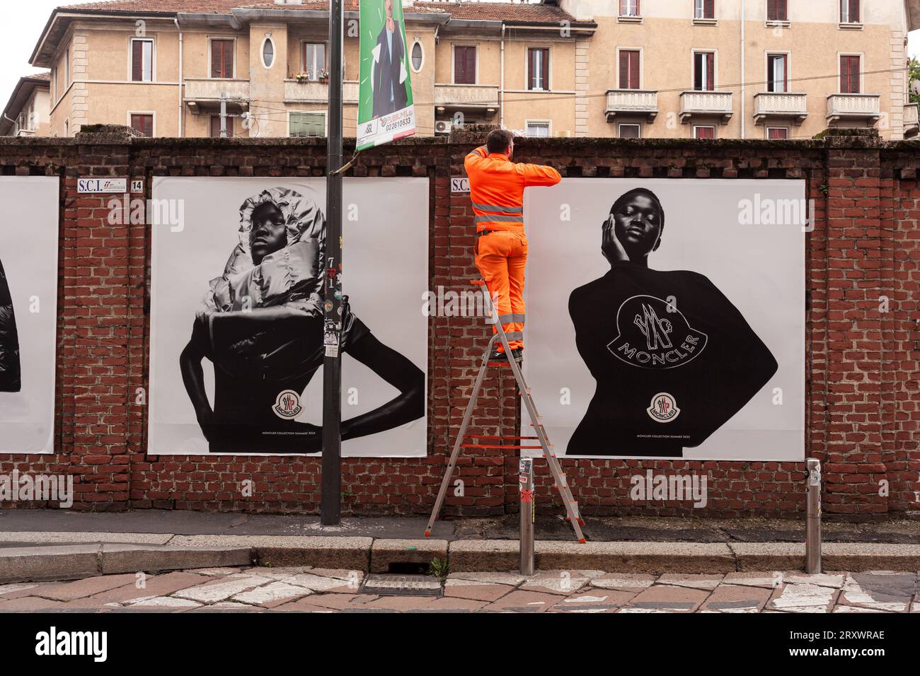 Milano, Italia - 21 aprile 2023: Un lavoratore sta mettendo sui muri dei manifesti della collezione Moncler del 2023 Foto Stock