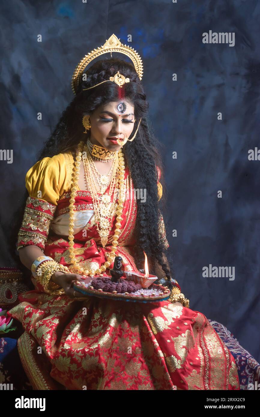 Ritratto della bellissima ragazza indiana di Durga Idol Agomoni Concept foto al coperto che indossa il tradizionale sari indiano, gioielli in oro e braccialetti. Maa Durga Foto Stock