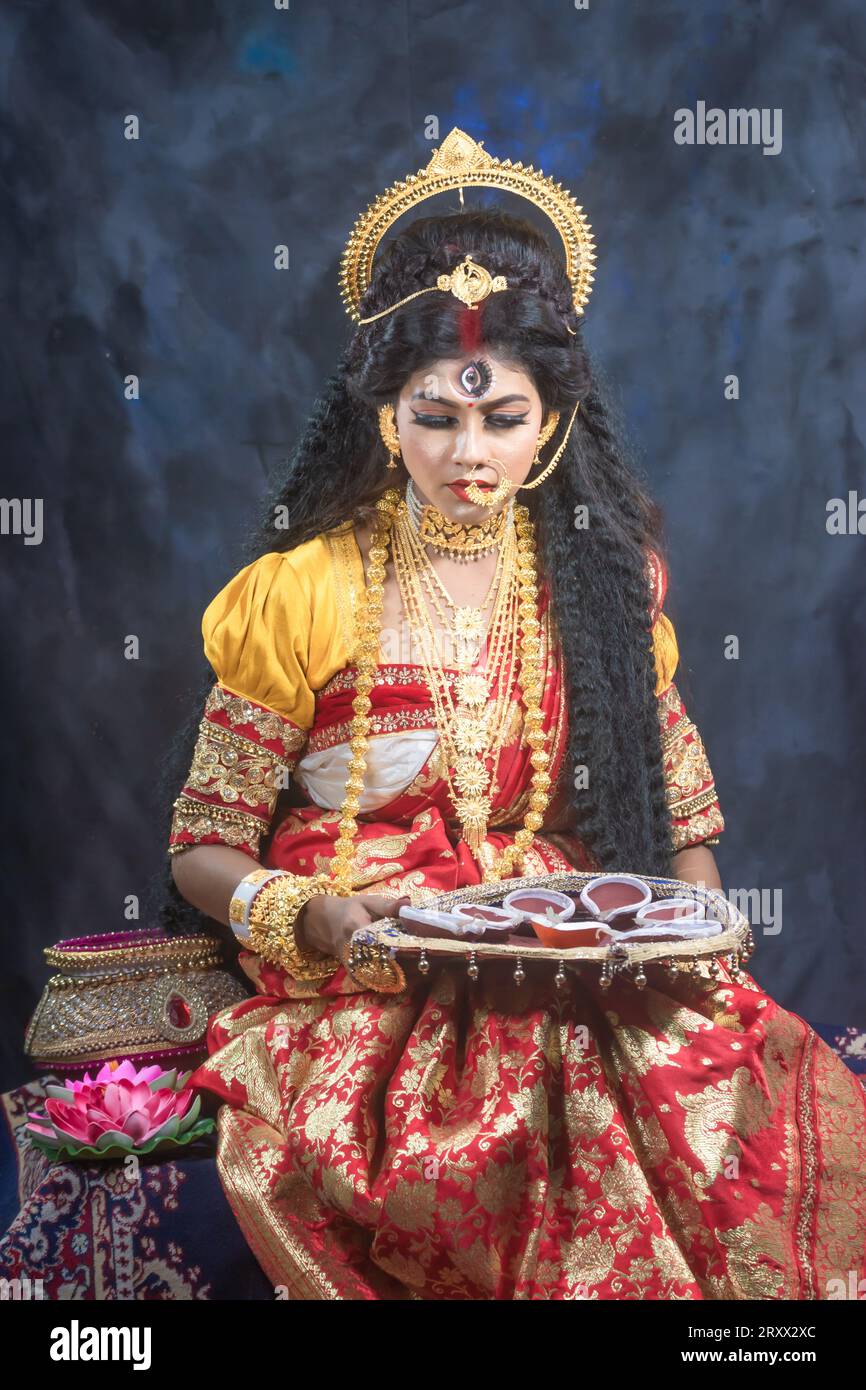 Ritratto della bellissima ragazza indiana di Durga Idol Agomoni Concept foto al coperto che indossa il tradizionale sari indiano, gioielli in oro e braccialetti. Maa Durga Foto Stock