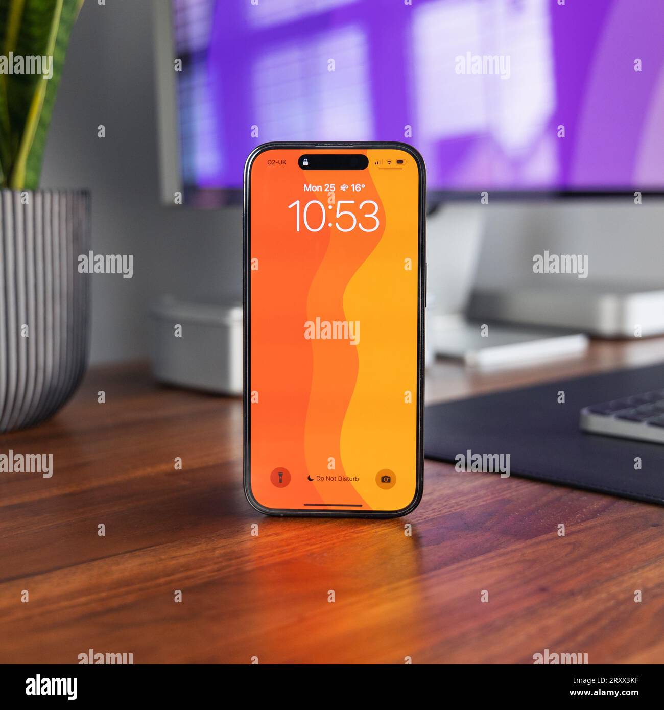 LONDRA - 25 SETTEMBRE 2023: Apple iPhone 14 Pro con carta da parati arancione su legno per ufficio domestico con configurazione minima della scrivania Foto Stock