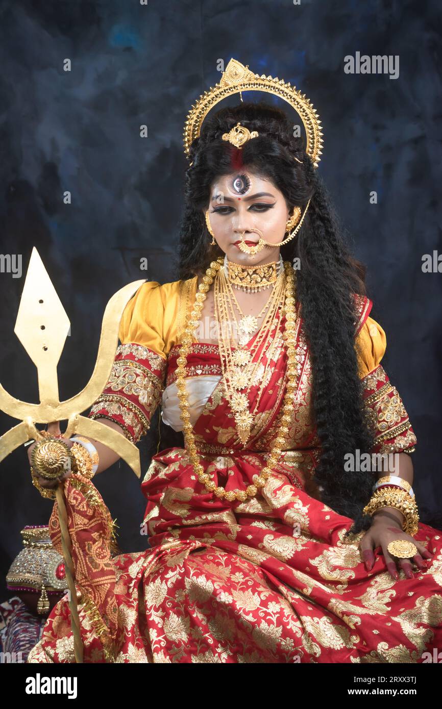 Ritratto della bellissima ragazza indiana di Durga Idol Agomoni Concept foto al coperto che indossa il tradizionale sari indiano, gioielli in oro e braccialetti. Maa Durga Foto Stock