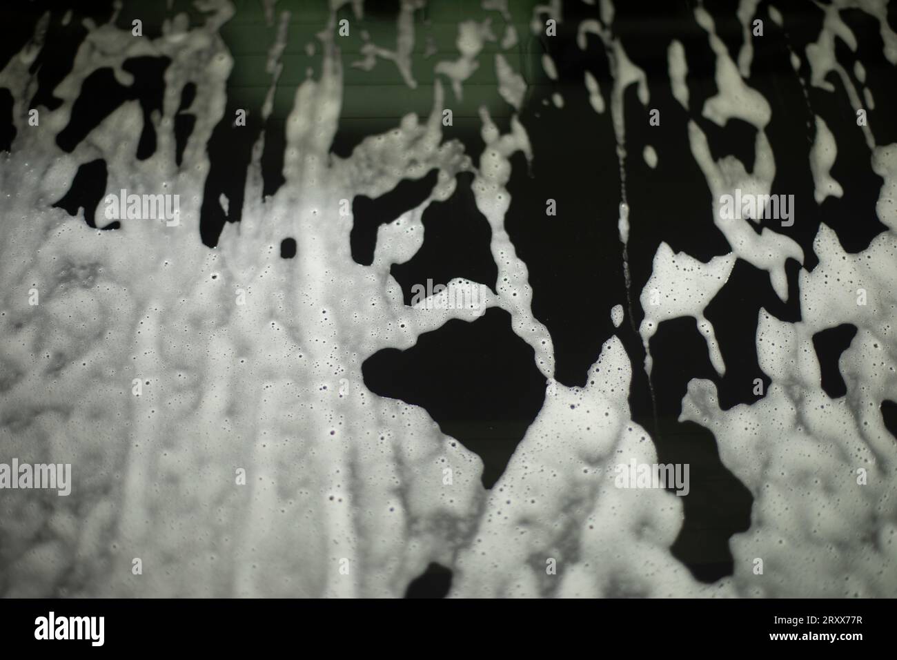 Schiuma di sapone su superficie scura. Risciacquo dello sporco dal vetro. Soluzione saponosa sull'auto. Consistenza della soluzione bianca. Foto Stock