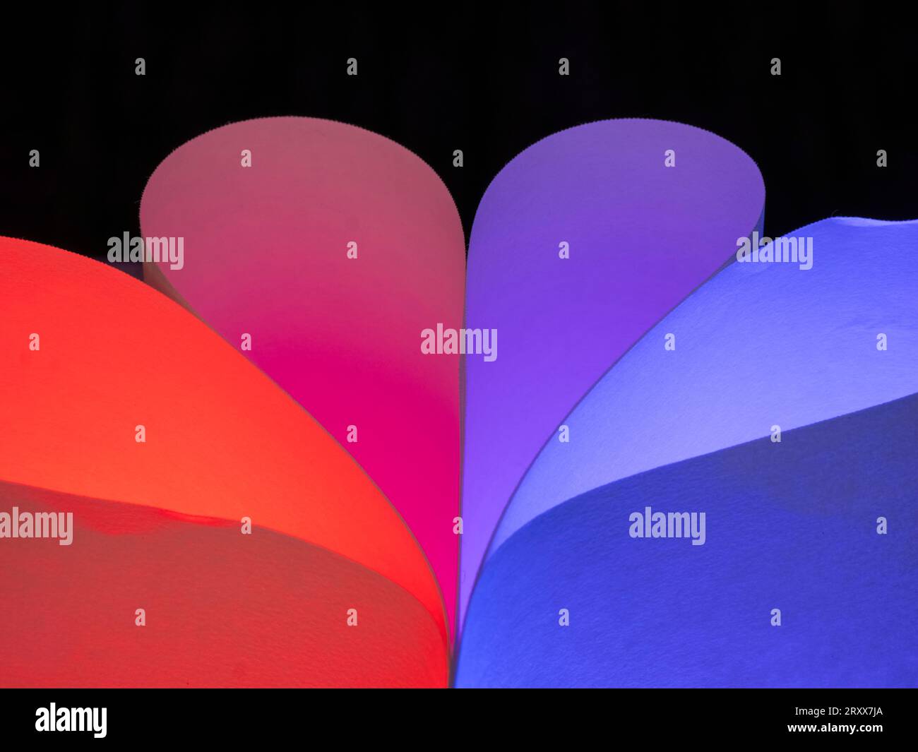 Primo piano delle forme curve di colore rosso e blu realizzate per normali fogli di carta bianca e luci colorate Foto Stock