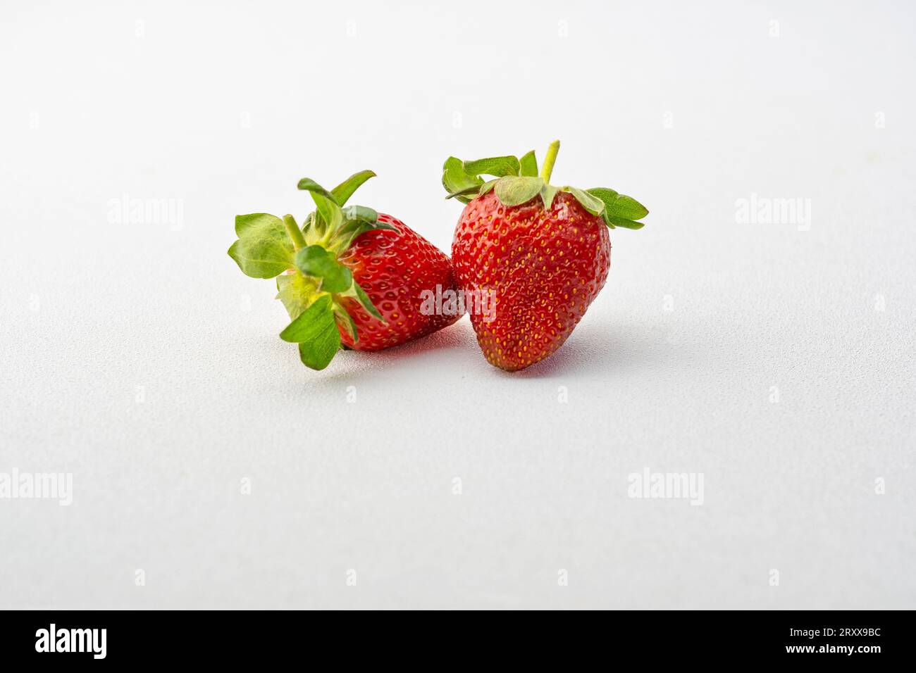 Due fragole lussureggianti, catturate in primo piano, sono splendidamente presentate su uno sfondo bianco incontaminato, il loro rossore succoso che invita a un morso. Foto Stock