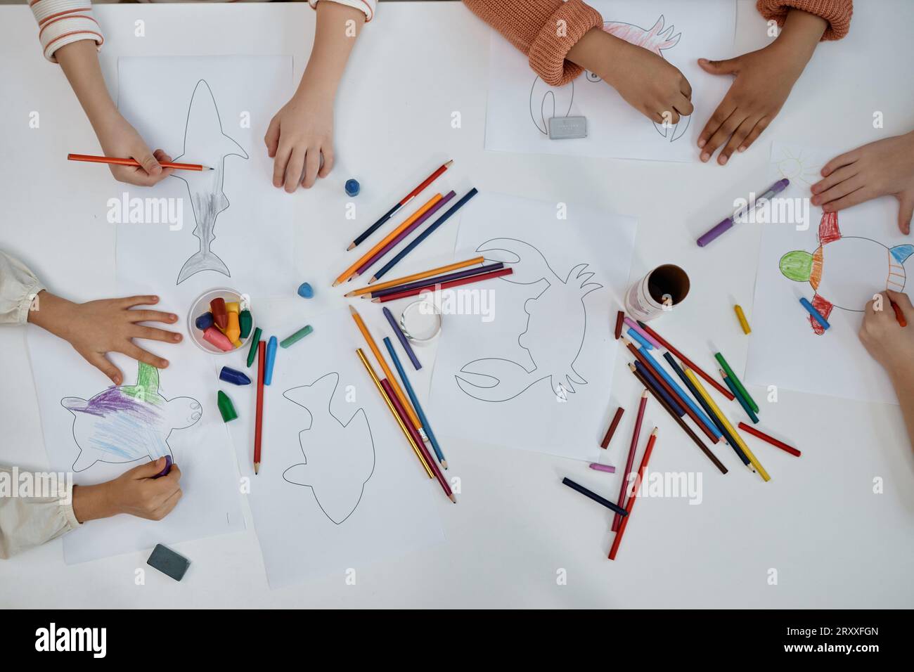 Vista dall'alto in primo piano di un gruppo multietnico di bambini che fanno arte e mestieri colorando le creature marine al tavolo della classe prescolare, spazio copia Foto Stock