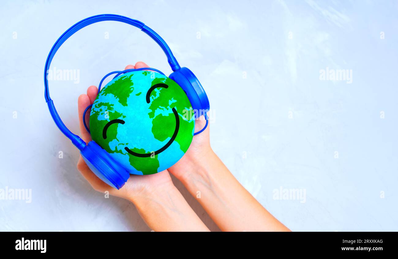 Le mani si stringono con un sorridente personaggio antropomorfo del globo mentre ascoltano la musica con le cuffie blu. Intrattenimento globale Foto Stock
