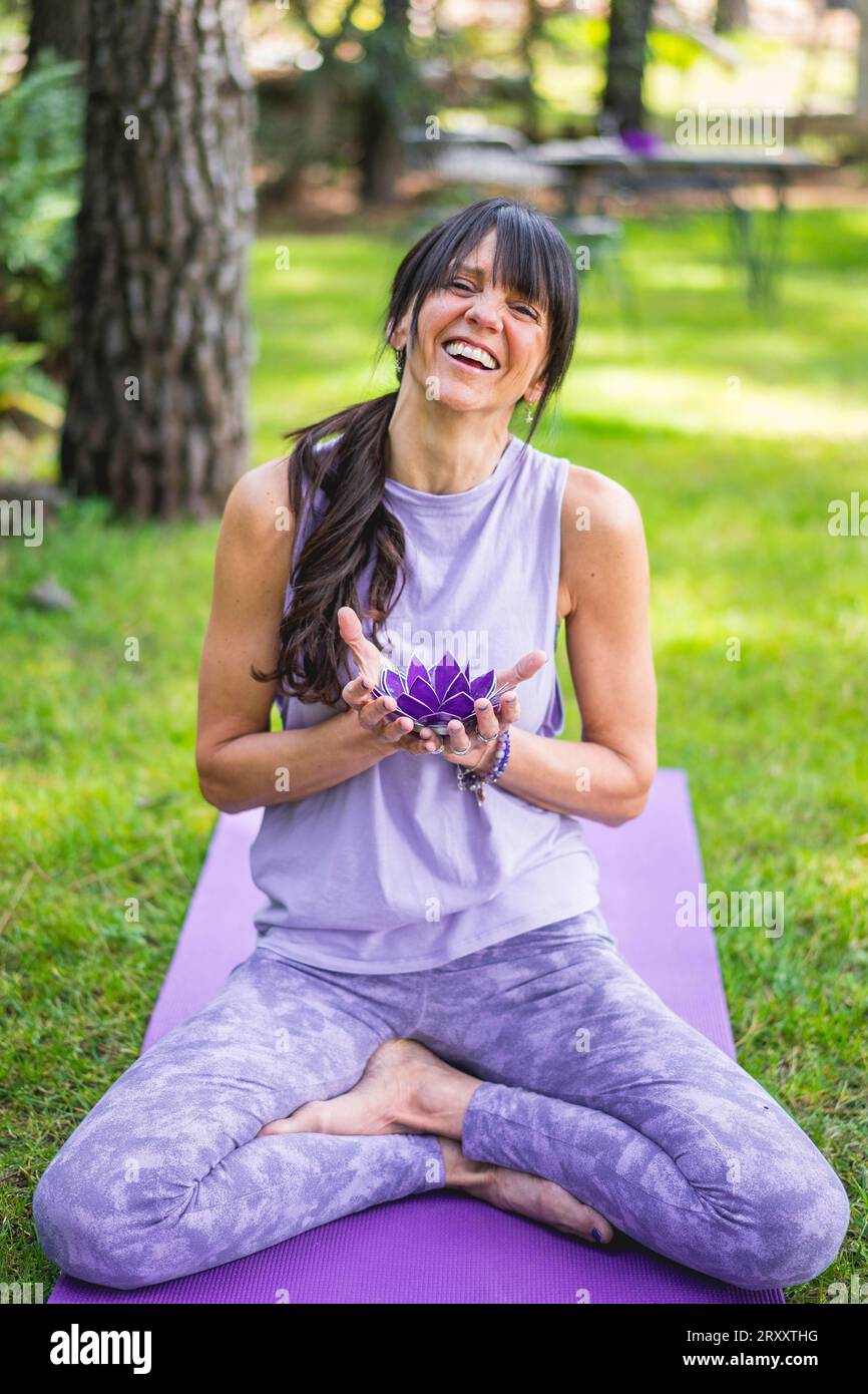 Donna felice seduta in posa di loto e con in mano un loto di vetro viola mentre ride Foto Stock