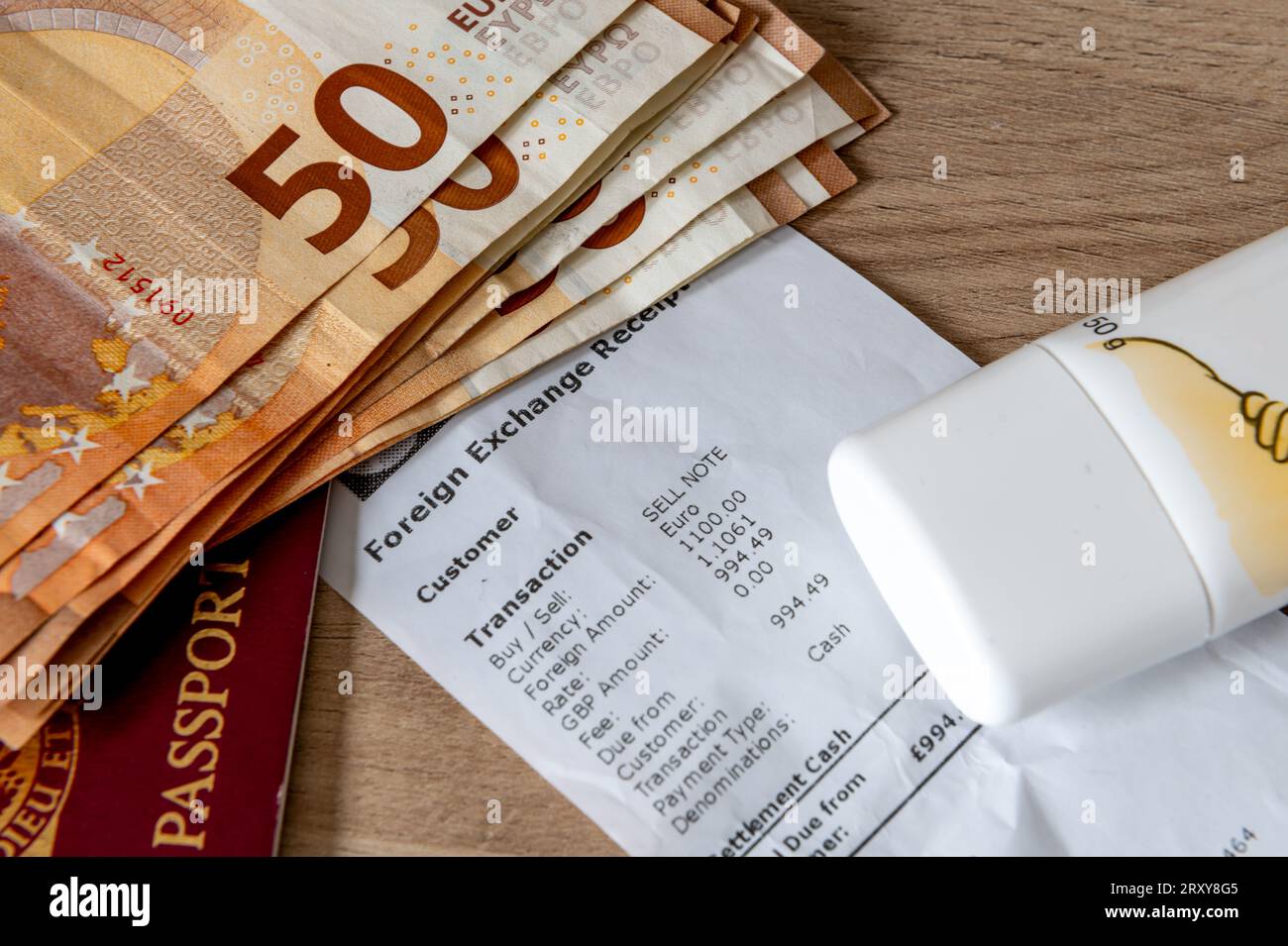 Un concetto di viaggio, vacanza e scambio di denaro con banconote in euro, un passaporto, crema solare sopra una ricevuta di cambio valuta. Foto Stock