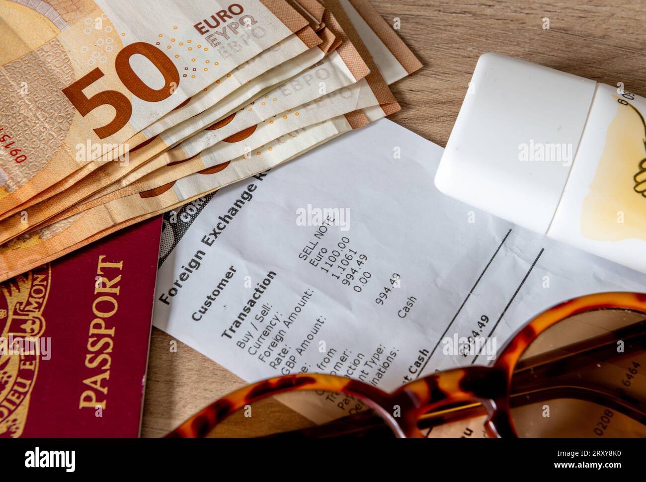 Un concetto di viaggio, vacanza e scambio di denaro con banconote in euro, passaporto, crema solare e occhiali da sole sopra una ricevuta di cambio valuta. Foto Stock