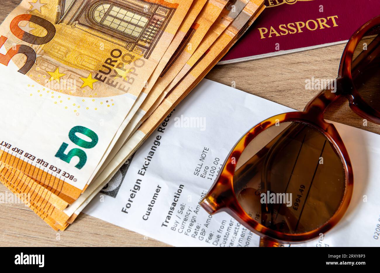 Un concetto di viaggio, vacanza e scambio di denaro con banconote in euro, passaporto e occhiali da sole sopra una ricevuta di cambio valuta. Foto Stock