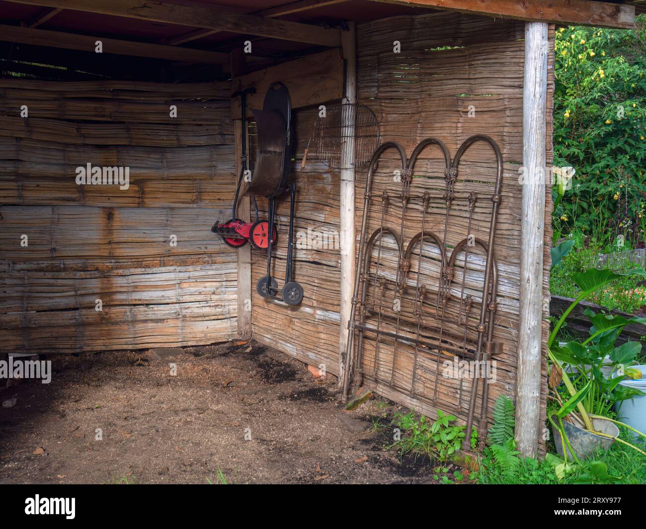 Un rasaerba manuale, una griglia nera di base e un letto d'epoca appeso a un muro di canna in un capannone rustico, in una fattoria vicino alla città di Villa de Leyva. Foto Stock