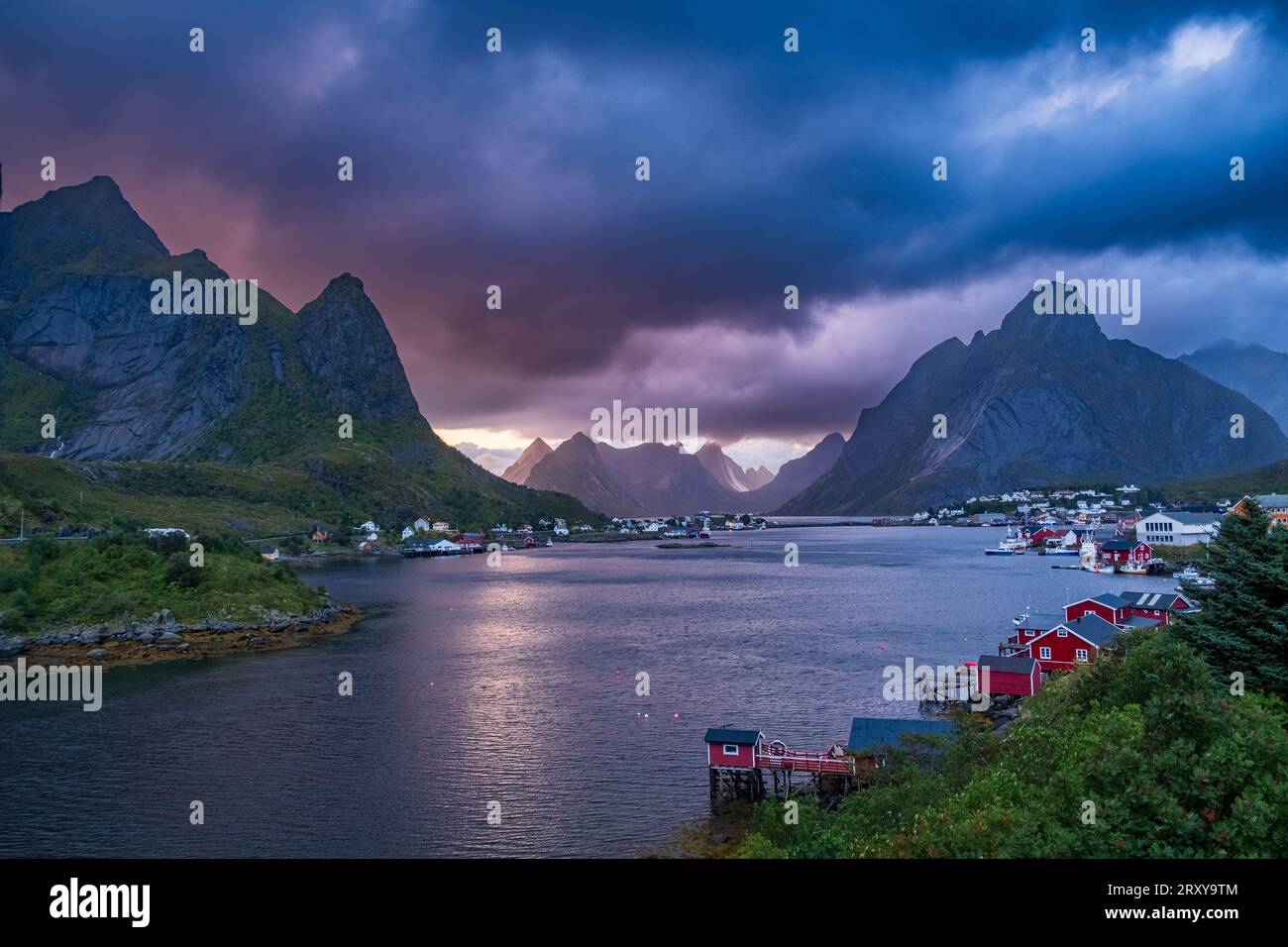 Pittoresco villaggio di Lofoten con tradizionali palafitte e una catena montuosa sullo sfondo. La scena è immersa nella luce del sole ed è accompagnata Foto Stock