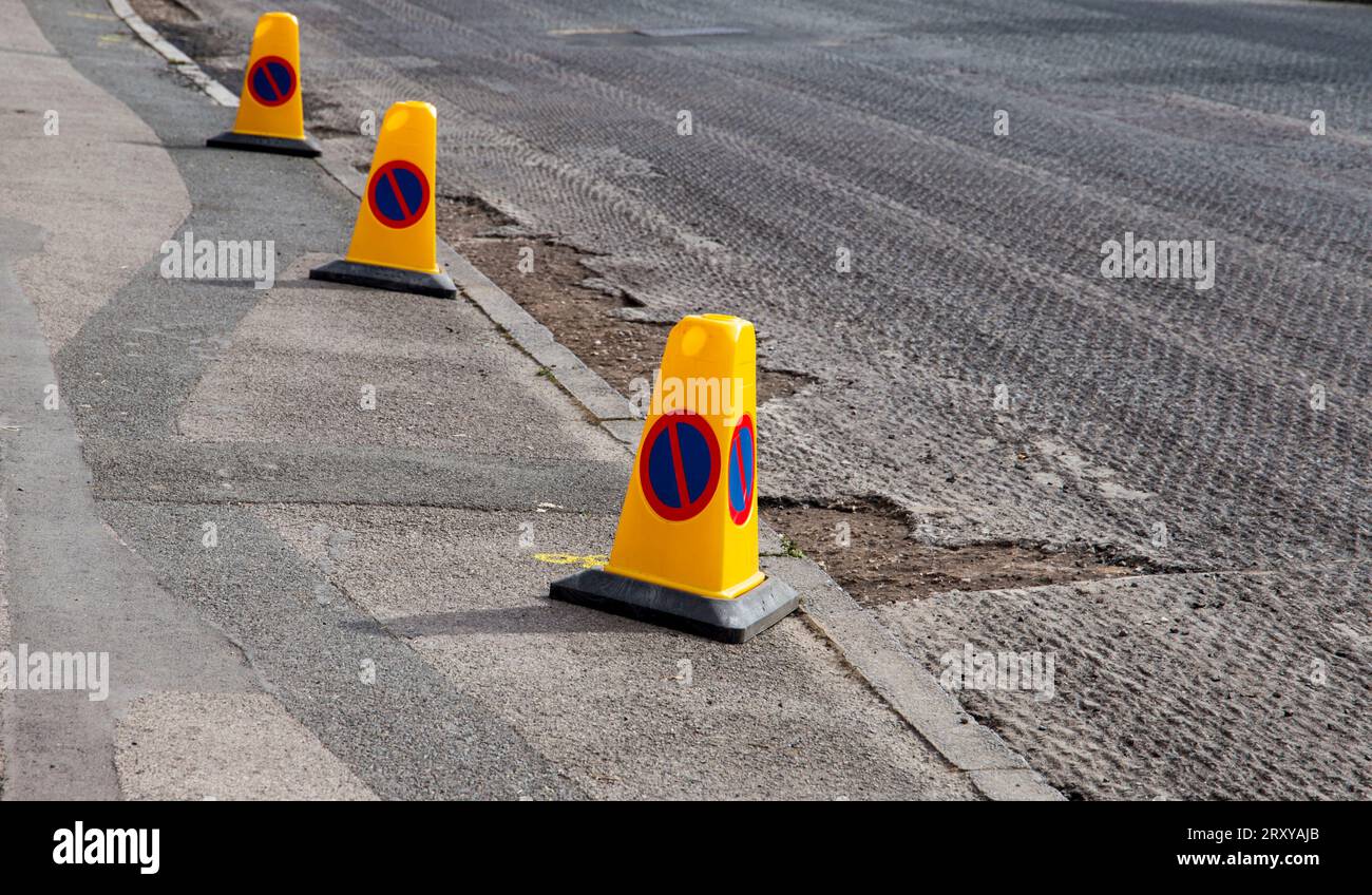 Fila di coni di parcheggio gialli non posti lungo una strada con pavimentazione parzialmente ripavimentata e marciapiede pedonale Foto Stock