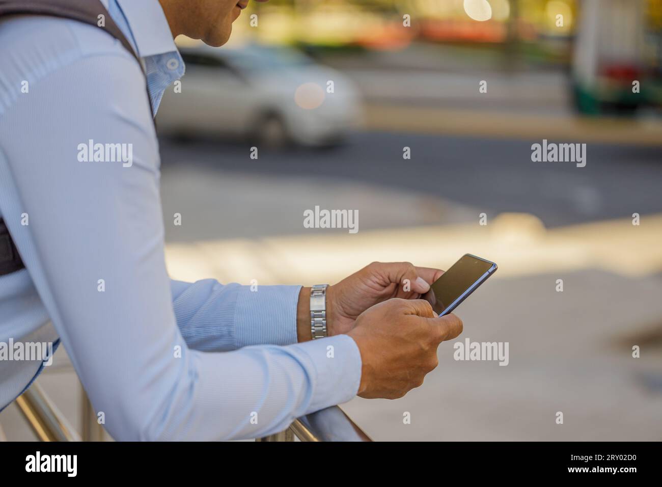 Primo piano di un uomo latino in camicia appoggiato su una ringhiera usando il suo cellulare. Foto Stock