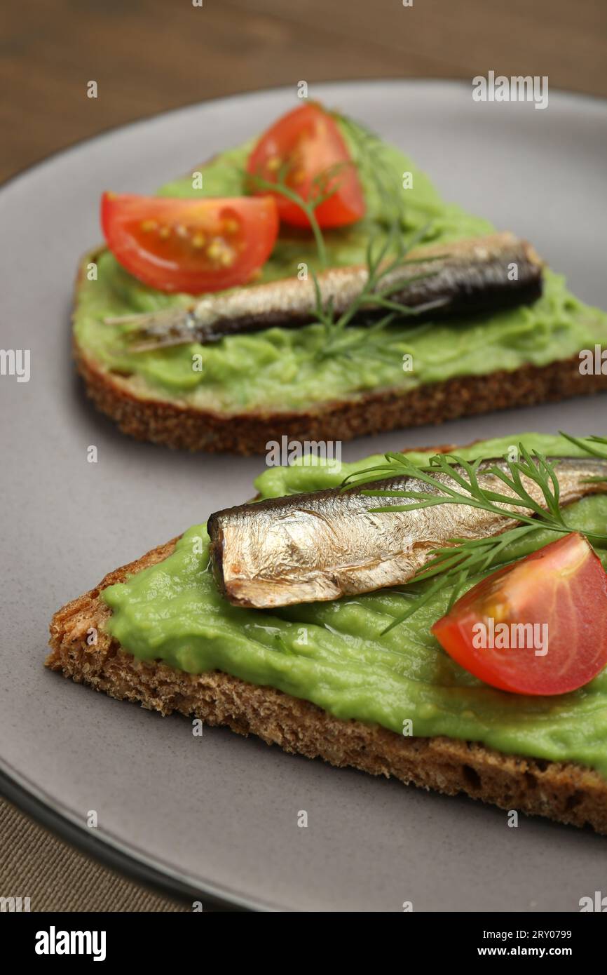 Deliziosi sandwich con spratti, pomodori, purea di avocado e aneto sul tavolo, primo piano Foto Stock