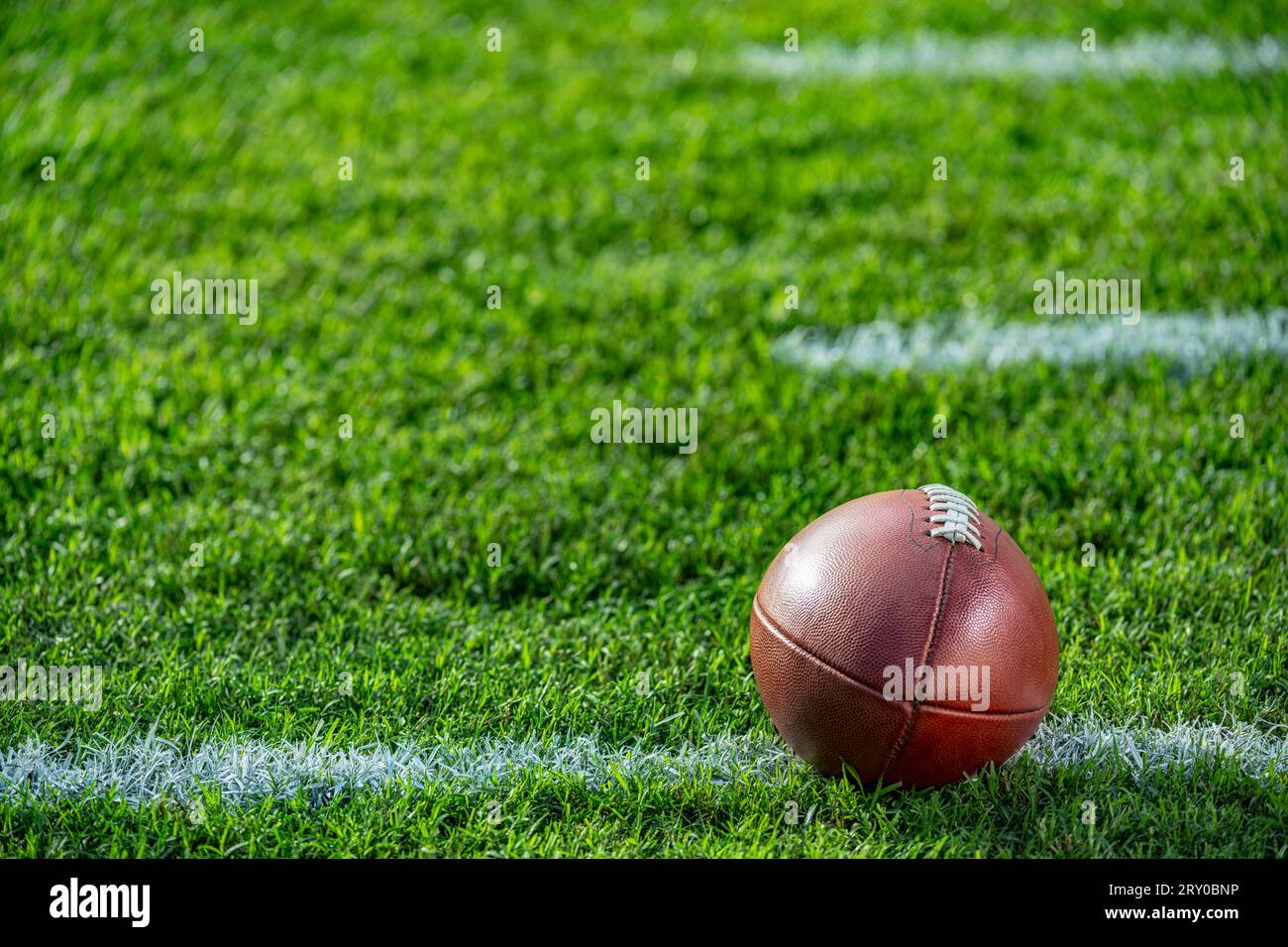 Vista ravvicinata da un angolo basso di un football americano in pelle seduto nell'erba su una linea bianca del cortile con segni di hash sullo sfondo. Foto Stock