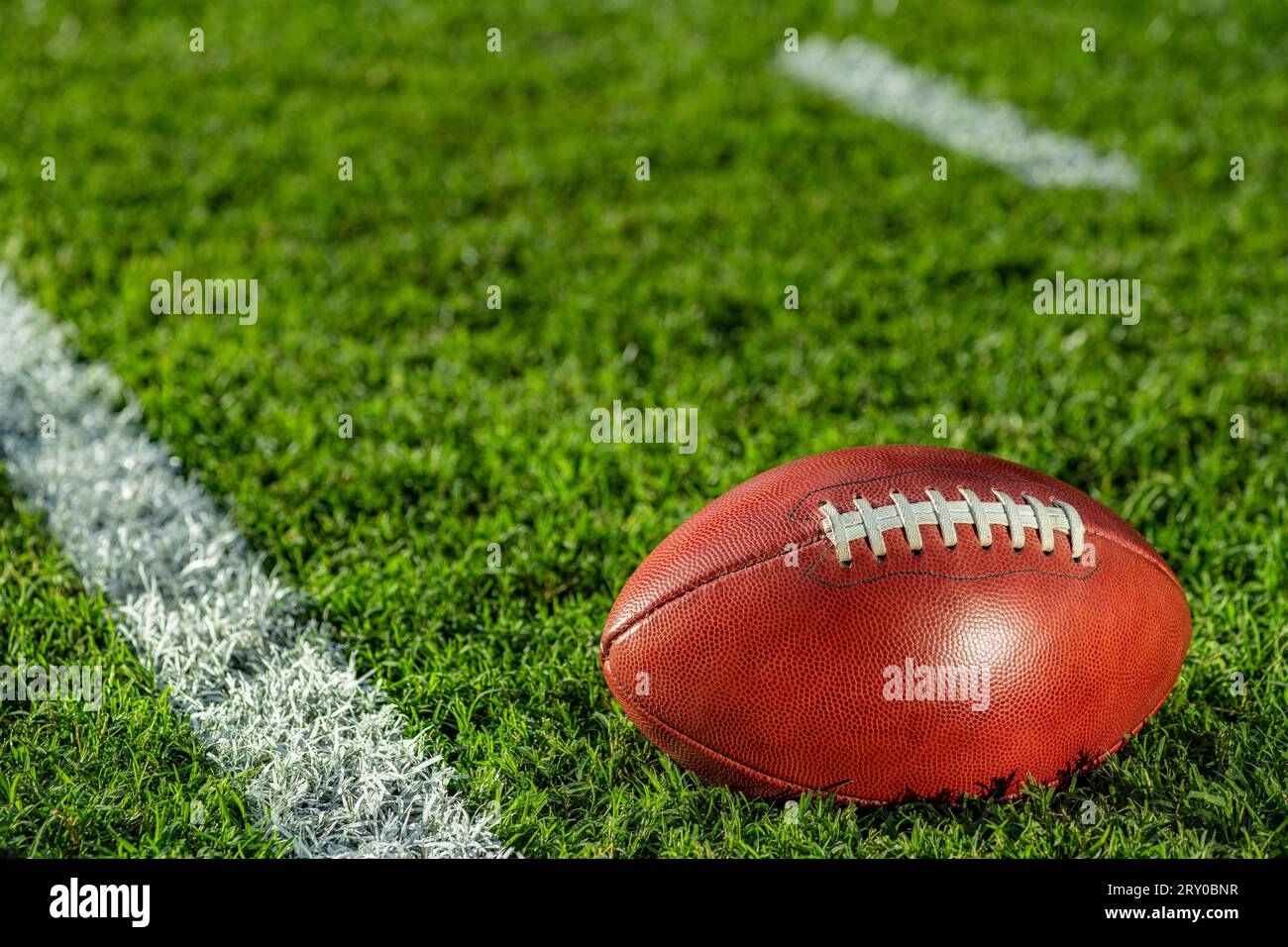 Vista ravvicinata da un angolo basso di un football americano in pelle seduto nell'erba accanto a una linea bianca del cortile con segni di hash sullo sfondo. Foto Stock