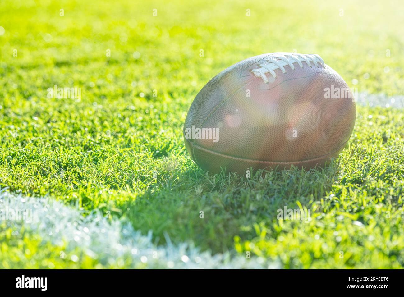 Vista ravvicinata da un angolo basso di un football americano in pelle seduto nell'erba accanto a una linea bianca del cortile con segni di hash sullo sfondo, riflesso dell'obiettivo. Foto Stock