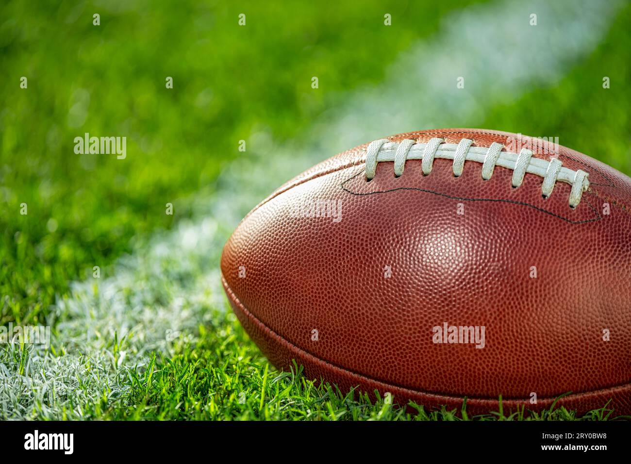 Vista ravvicinata di un football americano in pelle seduto nell'erba accanto a una linea bianca del cortile. Foto Stock