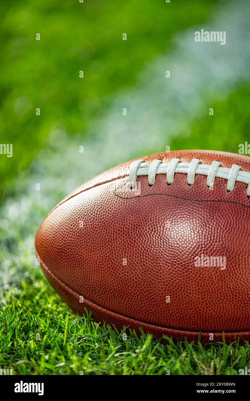 Vista ravvicinata di un football americano in pelle seduto nell'erba accanto a una linea bianca del cortile. Foto Stock