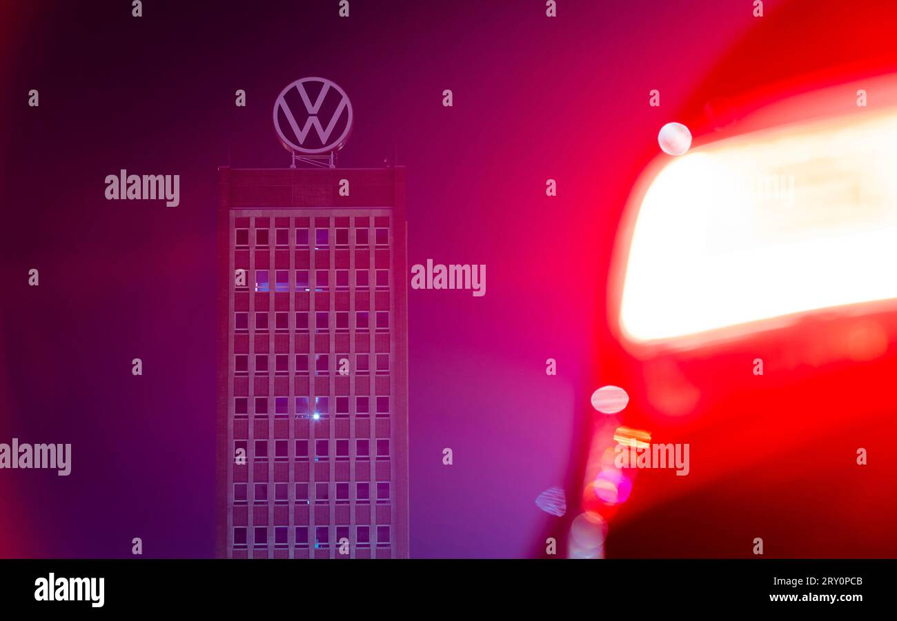27 settembre 2023, bassa Sassonia, Wolfsburg: Al mattino presto, il grattacielo del marchio presso la sede Volkswagen appare quasi completamente scuro dietro la luce di posizione posteriore rossa brillante di un'auto. Un malfunzionamento IT ha paralizzato l'infrastruttura centrale del gruppo Volkswagen. Foto: Moritz Frankenberg/dpa Foto Stock