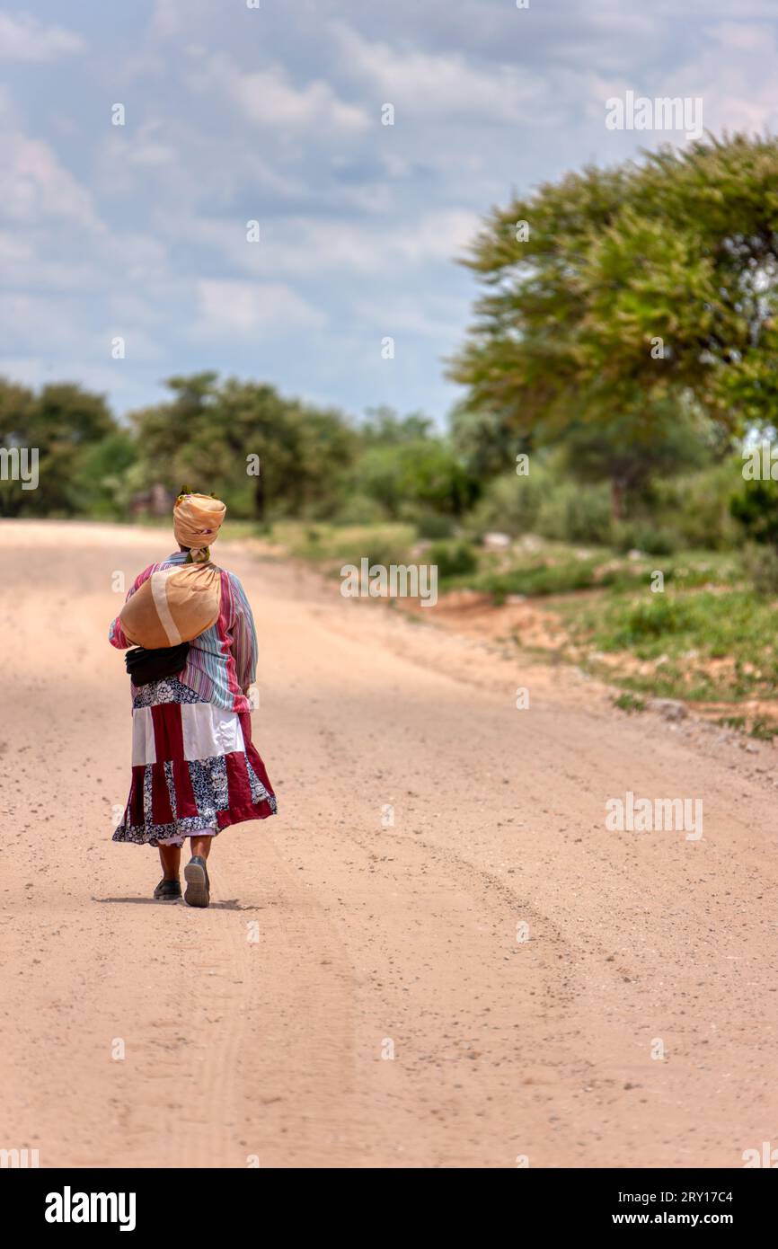 donna africana basarwa che cammina su una strada sterrata nel villaggio tradizionale Foto Stock