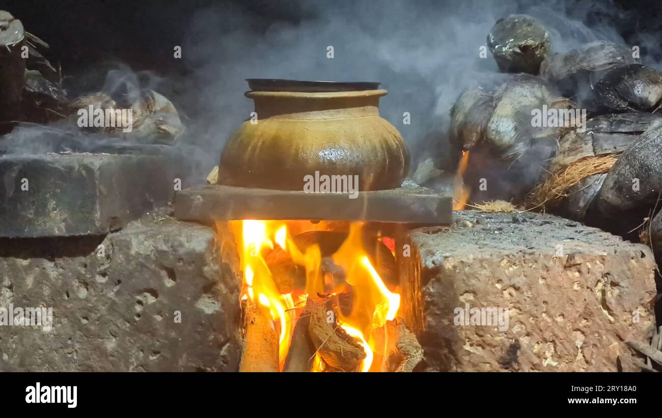 un bollitore marrone con cibo cotto e affumicato sotto il fuoco in una vecchia stufa tradizionale che brucia con legna da ardere Foto Stock