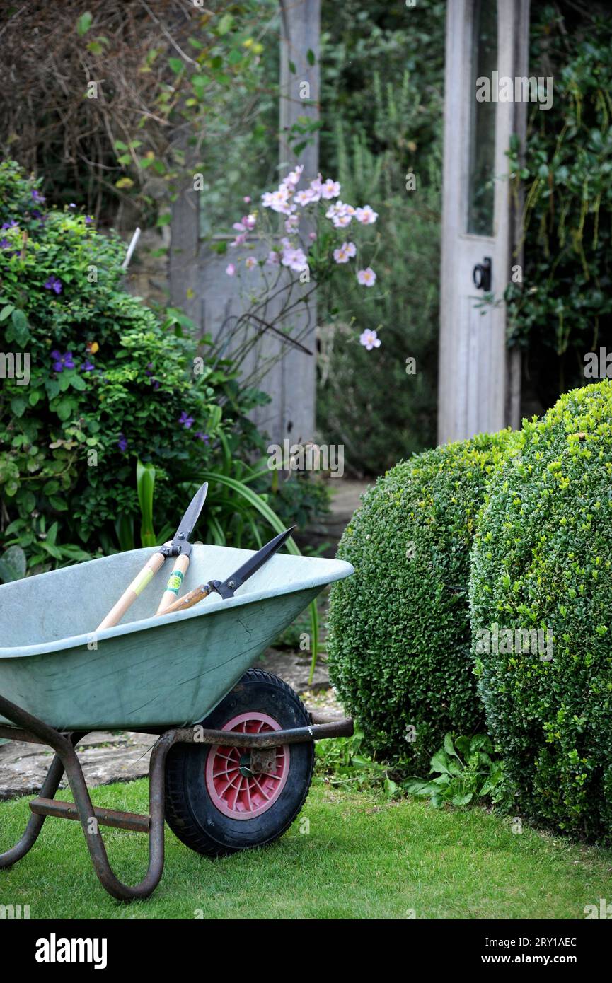 Cesoie per siepi scolpite e una carriola per il trasporto di giardinieri. Foto Stock