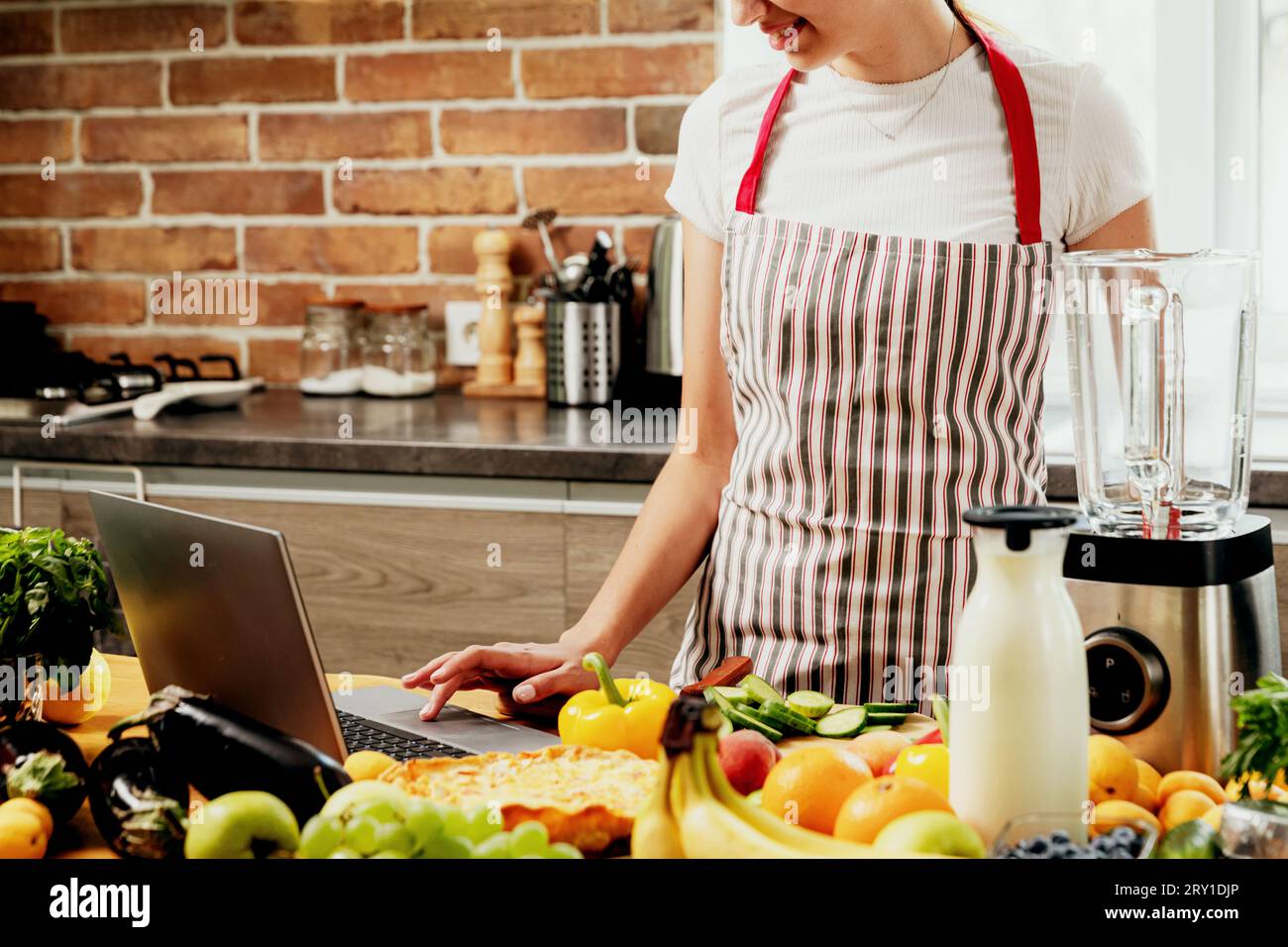 Donna che usa un notebook in cucina. Ragazza che tocca il touchpad con la mano, alla ricerca di una ricetta. Chef che usa pc, acquisti di cibo online su computer. Consegna Foto Stock