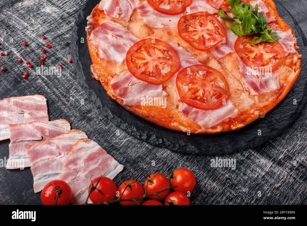 Pizza tradizionale italiana con mozzarella, prosciutto, pomodori, pepe, spezie di pepe e rucola fresca su una pietra e cinghiale di gesso nero graffiato Foto Stock