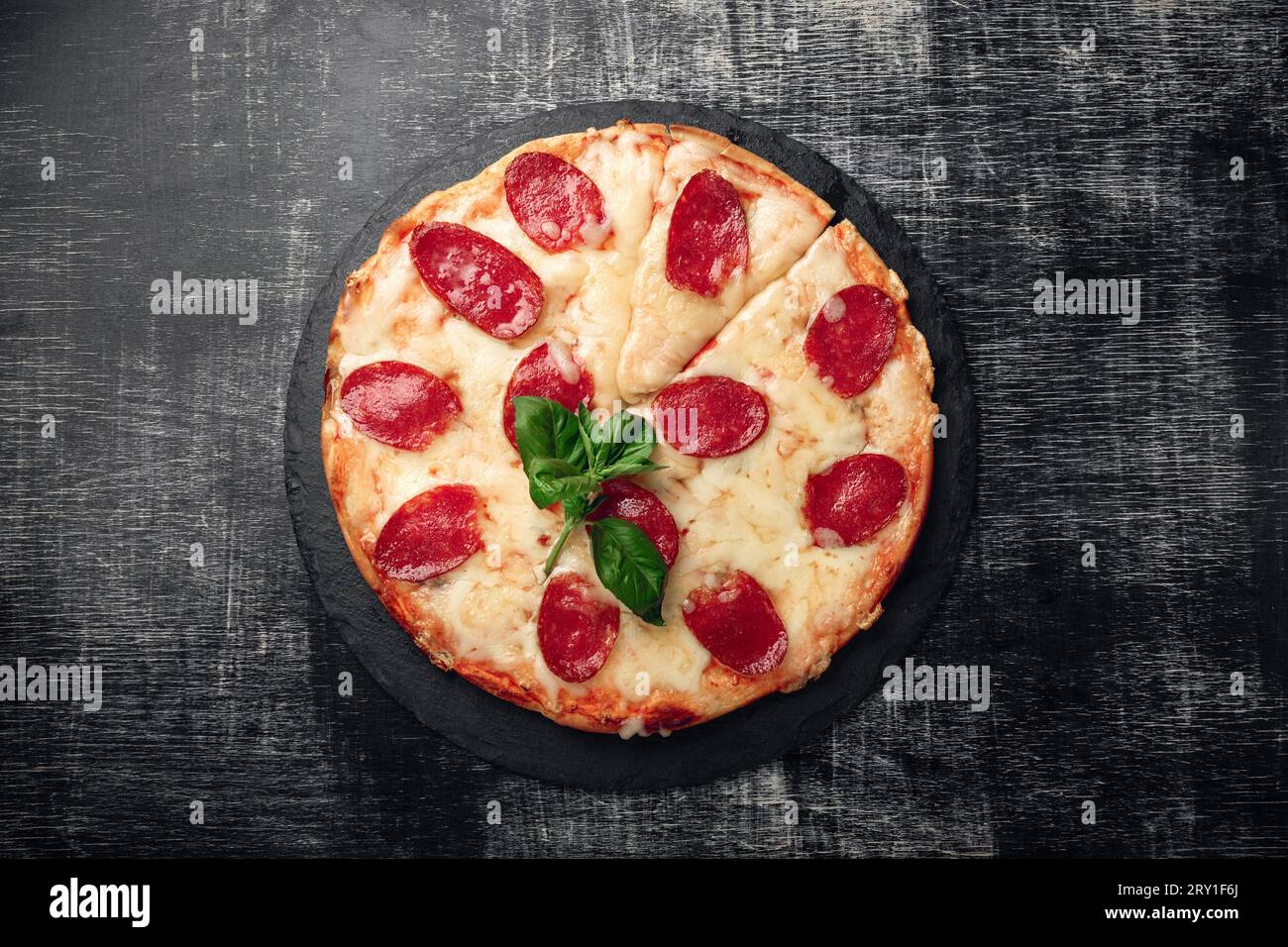 Pizza con formaggio e salame su pietra e gesso nero, vista dall'alto. Foto Stock