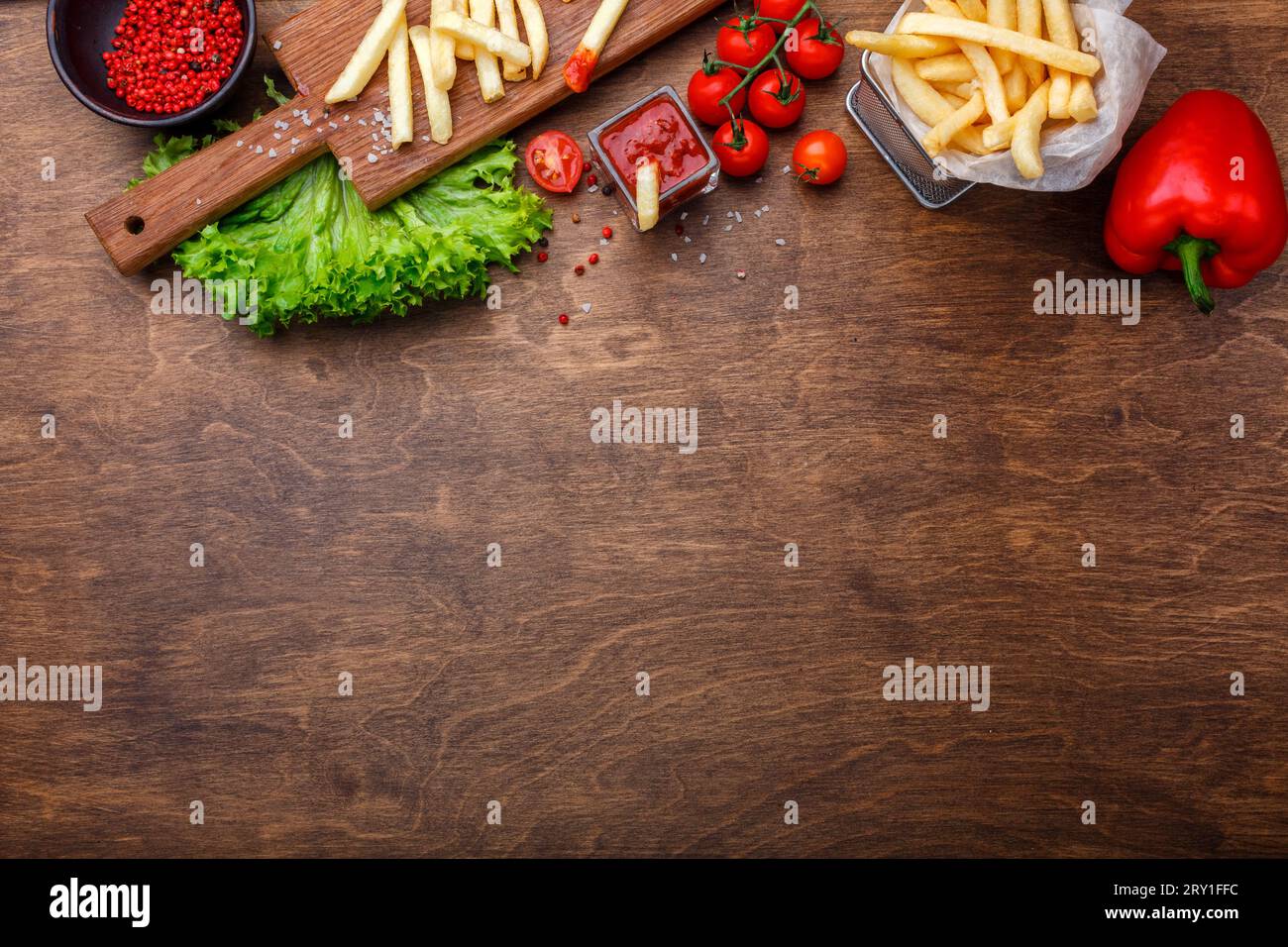 Patatine fritte in griglia con ketchup, insalata e pomodori ciliegini su tavola marrone di legno. Vista dall'alto con spazio per il testo. Foto Stock