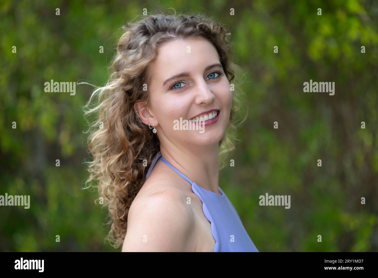 Ritratto della testa e delle spalle di una giovane donna caucasica sorridente con capelli biondi ricci e occhi blu, all'aperto in estate Foto Stock