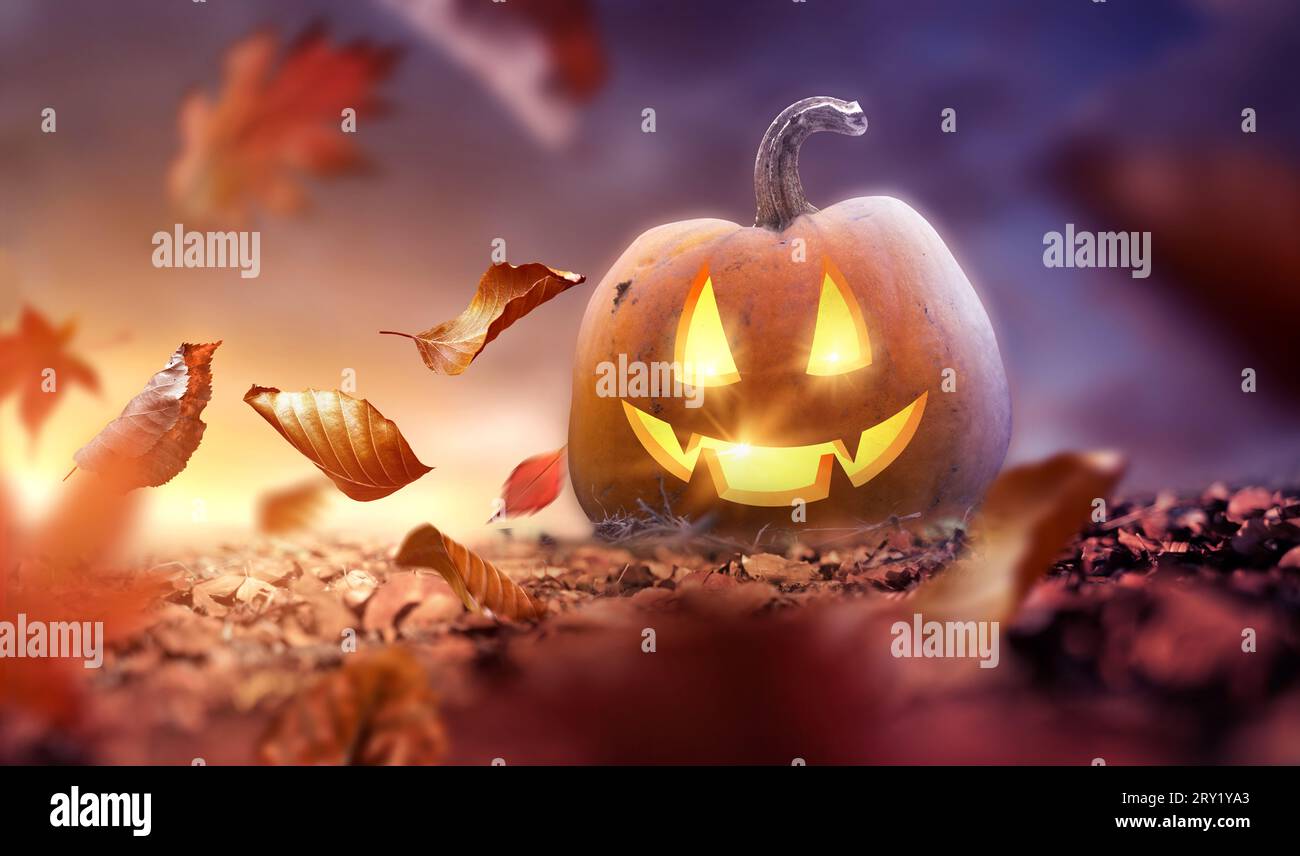 Autunno con foglie di alberi che soffiano acrosdi a terra con una lanterna Jack o che sorride. Concetto di Halloween. Foto Stock