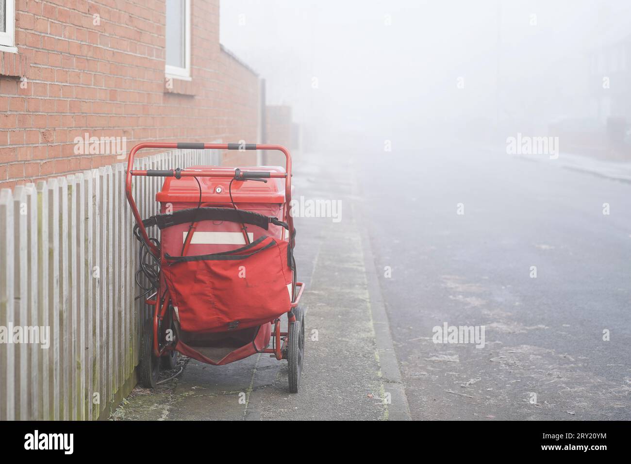 Il carrello postale della Royal mail è stato lasciato dal postino locale a fare il suo giro, isolato sul marciapiede di una strada residenziale in una nebbiosa mattinata invernale a gennaio. Foto Stock