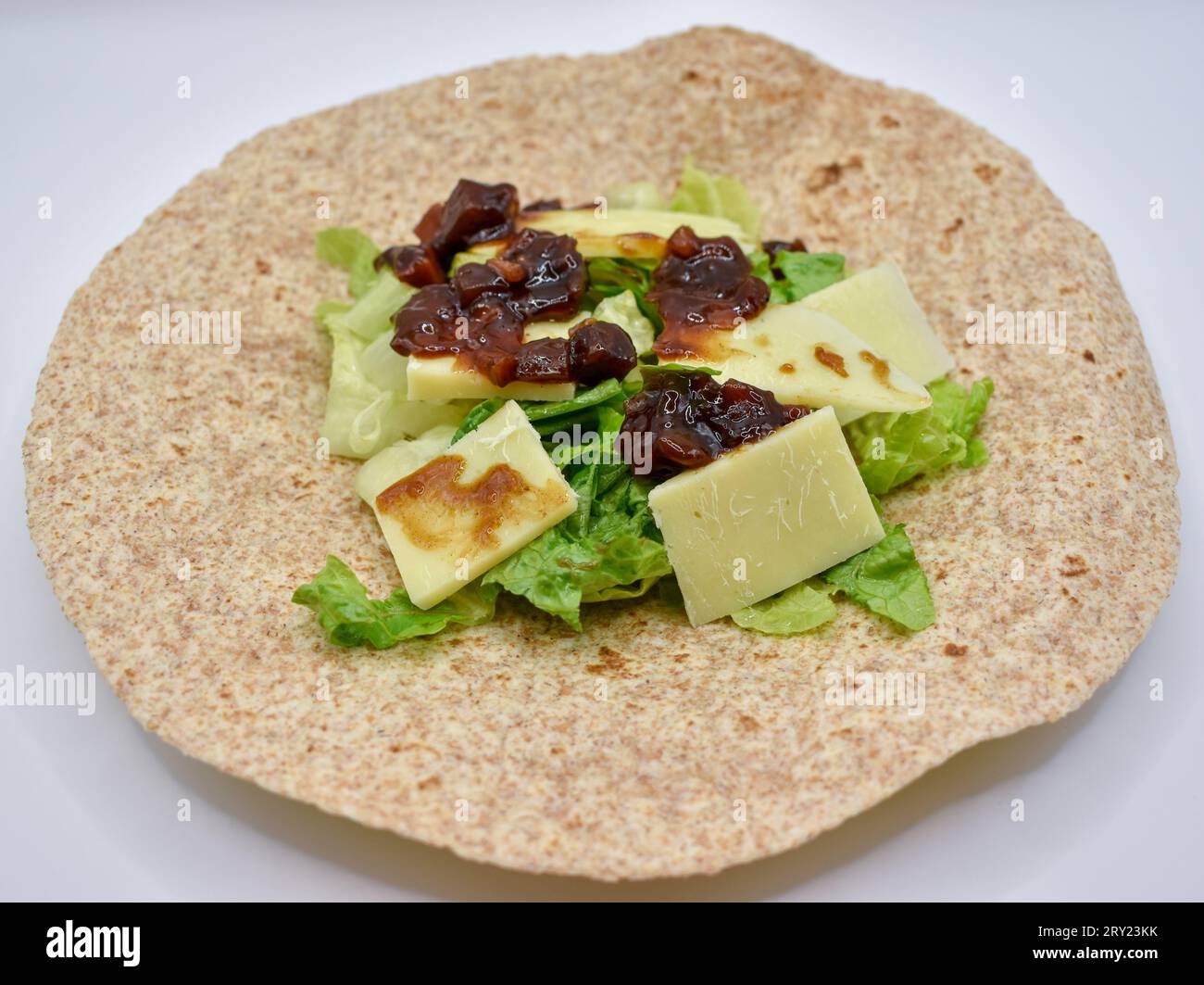 Una tortilla completa preparata per pranzo con formaggio cheddar a fette, chutney sottaceto e lattuga tritata. Foto Stock