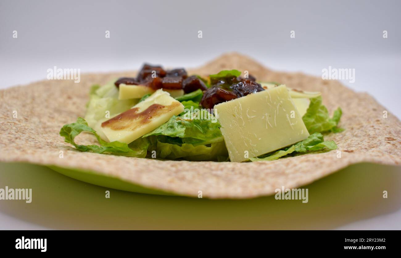 Una tortilla completa preparata per pranzo con formaggio cheddar a fette, chutney sottaceto e lattuga tritata. Foto Stock