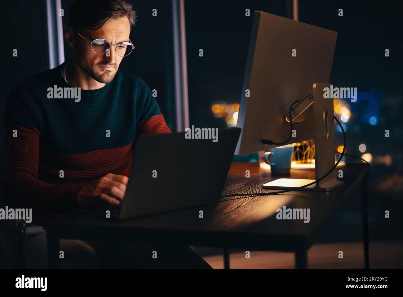 Web designer che lavora fino a tardi in un ufficio, utilizzando il suo laptop per completare un progetto. uomo d'affari seduto alla sua scrivania, che utilizza la tranquilla atmosfera notturna Foto Stock