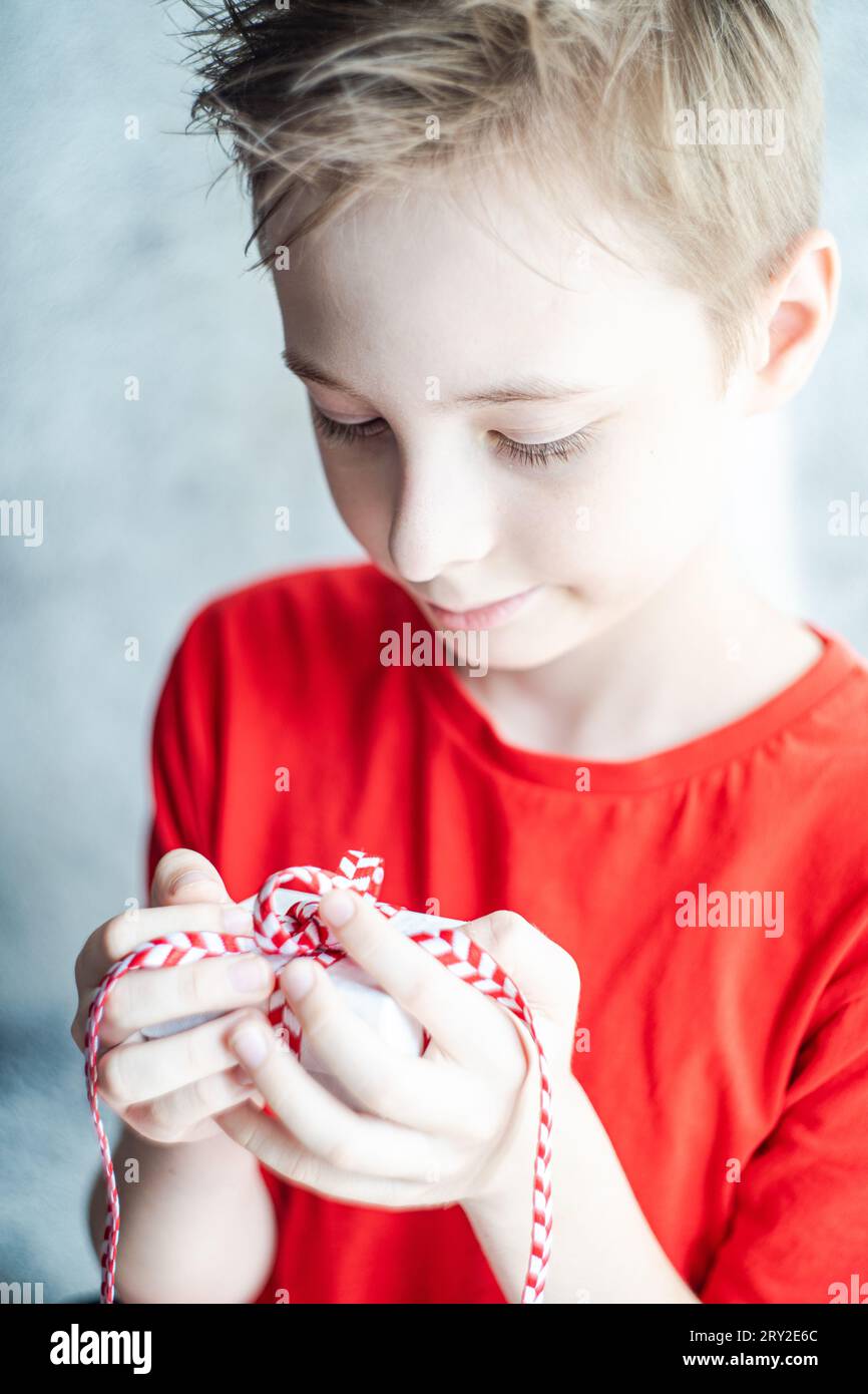 Bambino sfocato che tiene in mano una piccola confezione regalo con nastro rosso durante le celebrazioni natalizie su sfondo sfocato Foto Stock